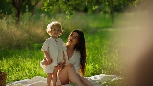 Woman and child sitting on blanket in a park