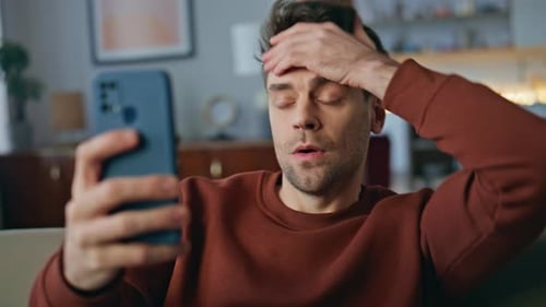 Man Looks Shocked While Using Smartphone at Home