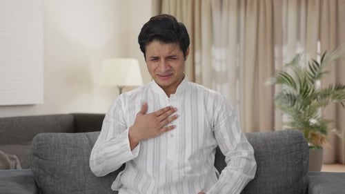 Man Experiencing Chest Discomfort While Sitting on Couch