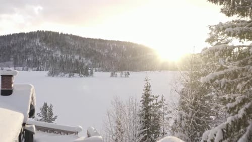 Bright Sun Shining Over The Mountains, Frozen Lake And Cabin During Winter. - aerial