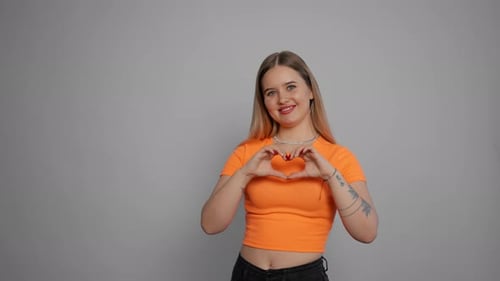 Mujer joven sonriendo ante la cámara cámara positiva con aspecto de niña feliz que muestra forma de corazón con las manos Enviar