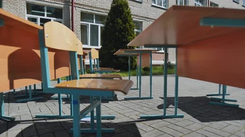 Empty School Desks and Chairs Standing Outdoors Near School Building on Sunny Summer Day Suggesting