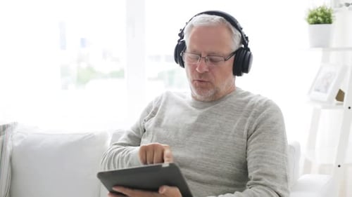 Joyful senior man at home enjoying music on his tablet with headphones