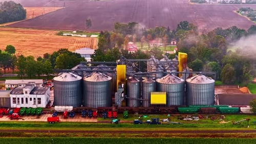 Aerial view of a large agriculture plant with harvested fields in the back and big silos next to a