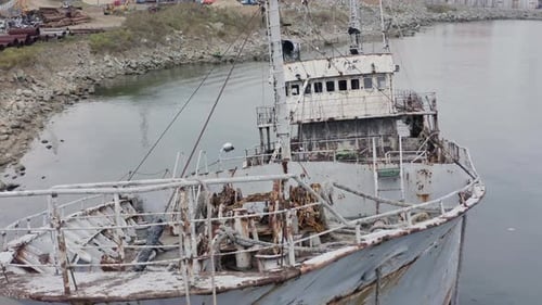 Rostgraues, halb untergetauchtes Schiffswrack, das an einem bewölkten, bewölkten Tag in Küstennähe vor Anker lag. Langsamer Luftbild