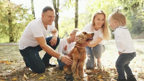 Cheerful young family have a rest in autumn park together and petting dog