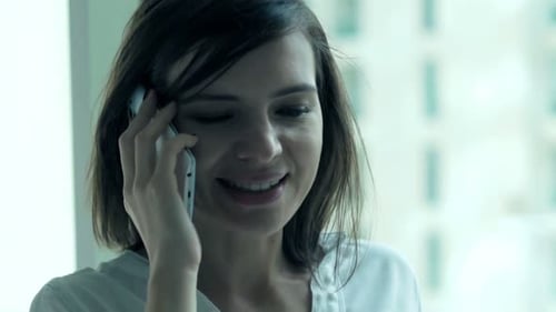 Young businesswoman chatting on cellphone in luxury office overlooking cityscape