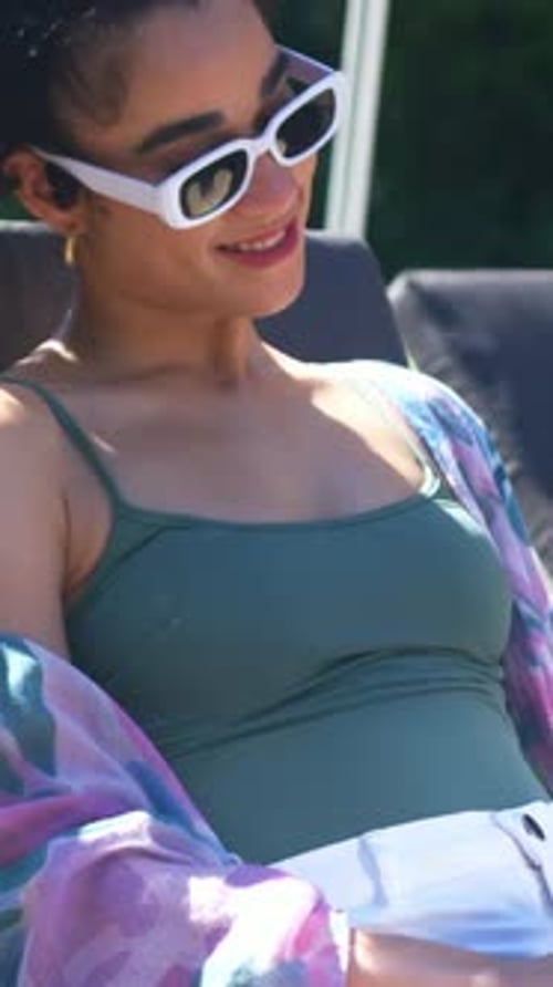Vertical video: Camera panning woman reclining on lounger, relaxing and adjusting wrap and shades
