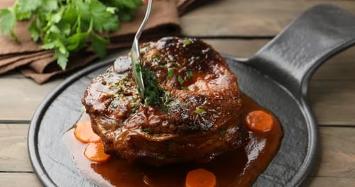 Woman adding pesto sauce to traditional ossobuco dish at wooden table, closeup