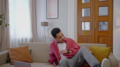 Charismatic African Guy in Skillful Dance Moves Freely to Music Sits Down on Sofa Turns on Laptop