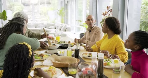 After grandma passing salad bowl, African American man raising fork, joining chat at dining table