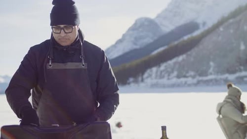 Man Prepares Food Outside in Snowy Mountain Setting