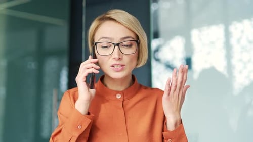 Close up of angry young blonde woman quarreling talking on smartphone while sitting at workplace at