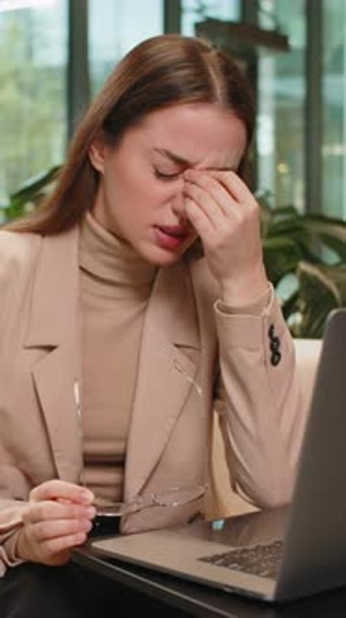 Overworked Businesswoman Suffering From Eye Strain and Headache Working on Laptop in Office Lobby