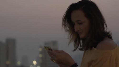 Young Woman with Smartphone Drinking Cocktail Sitting on Terrace in Bar At
