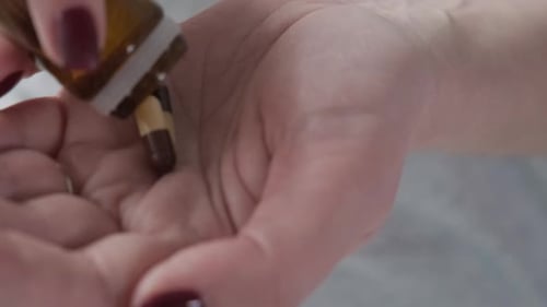 Woman pours capsule pills into hand close-up