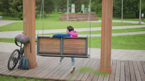 Serene Woman Sitting on Swing Beside Bicycle in Tranquil Park Scene Calm Scene of Woman Resting on