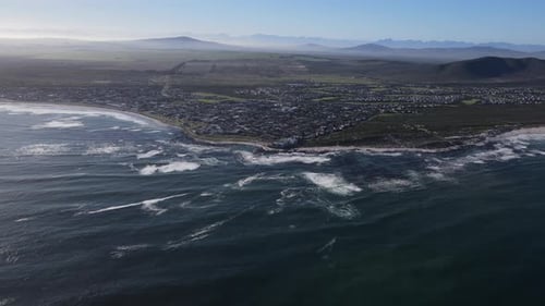 Drohne fliegt über den Ozean mit einer Küstenlandschaft mit Stadt- und Bergblick