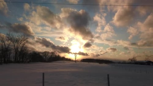 Wide slow moving shot of beautiful sunset sky overlooking farmer's fields clad in snow