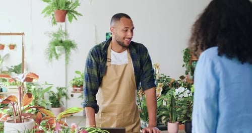 Cheerful handsome young man florist selling flower pot. Woman buys spring housplants in flower store