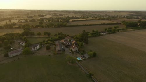 Golden hour over rustic countryside village with stone houses and trees.