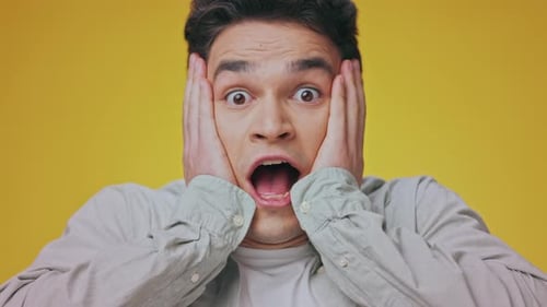 Surprised Man with Hands to Face Against Yellow Background
