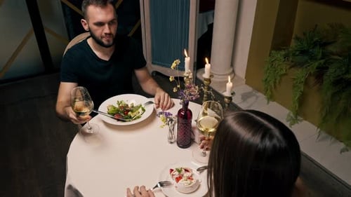 Portrait of a young guy with a beard eating salad in an Italian restaurant during a date with girl