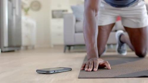 African american man doing mountain climbers using smartphone in living room, slow motion