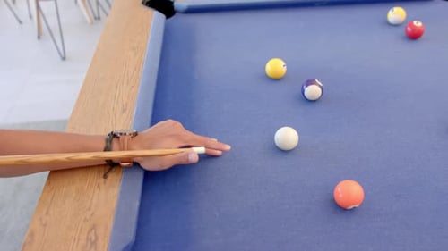 Playing billiards, person aiming cue stick at balls on pool table