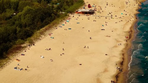 Sandstrand mit sanften Wellen und verstreuten Menschen Küstenrand, gesäumt von Wald und Grün, Küste