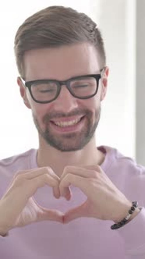 Smiling Man Making Heart Shape With Hands Indoors