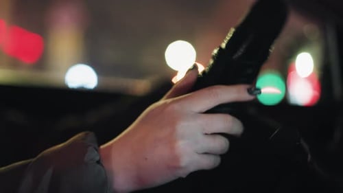 CloseUp of Woman Tapping Finger on Steering Wheel at Night with Blurred City Lights