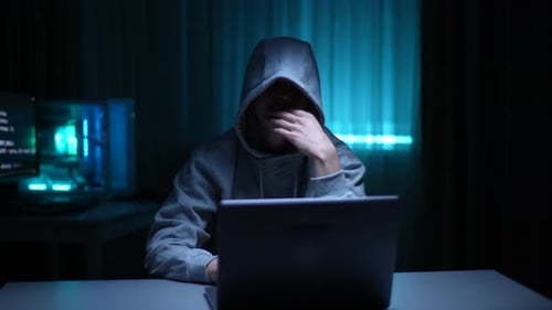 Hooded Person Working on Laptop in Dark Room