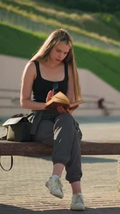 Woman Reading Book on Park Bench in Daytime