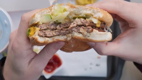 Man holding bitten burger in hands. Male eating hamburger in fast food restaurant