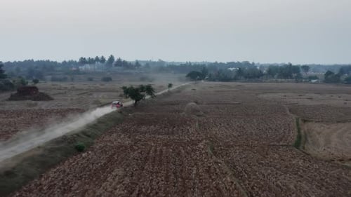 Red Car Speeding Down Dirt Road Through Rural Agricultural Fields.
