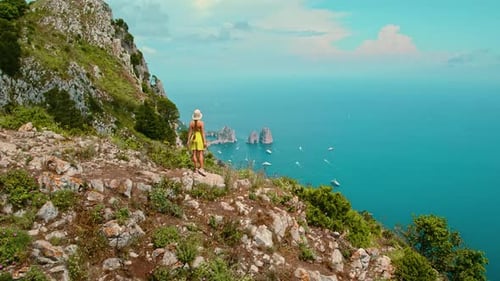 Tourist stands on the cliff's edge and gazing over Capri Island. Green lush vegetation, rocky coast,
