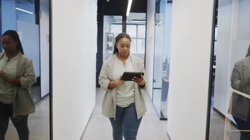 Happy african american casual businesswoman using tablet walking in office corridor, slow motion