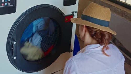 Woman Watches Clothes Wash in Laundromat Machine