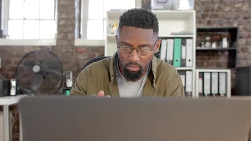 Focused african american casual businessman using laptop and having lunch in office in slow motion