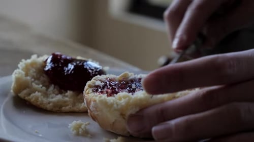Plan rapproché d'une main féminine étalant une cuillerée de confiture sur deux plats traditionnels faits maison fraîchement sortis du four