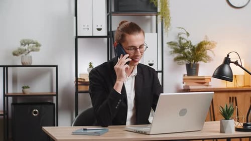Young Adult Smiling and Talking on Phone at Desk