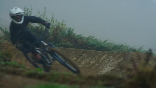 A downhill mountain biker performs a turn in the fog