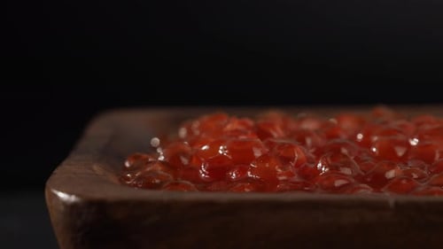 Wooden cup with red caviar on a black slate stone.