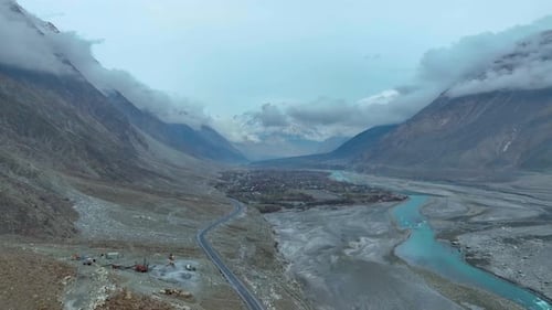 Drone flies high above a deserted street in nomal gilgit - Large riverbed and mountains with clouds