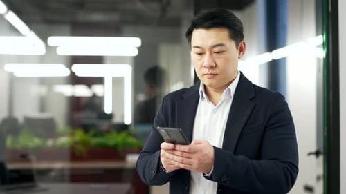 Serious asian businessman is using the phone while standing in business office