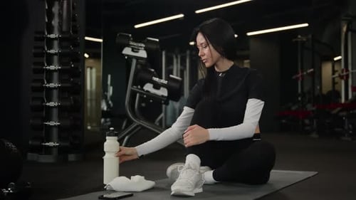 Athletic Woman Drinking Water, Using Cellphone in Gym