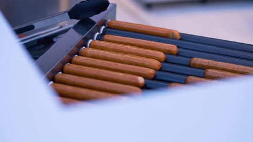 Hot dogs are cooking on a grill in an urban park.