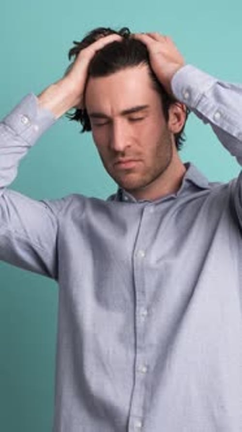 Frustrated Man Suffering From Headache in Blue Studio