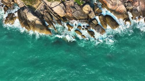 Aerial drone view of foamy waves breaking on a rocky shore.